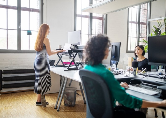 Personen im Büro an höhenverstellbaren Tischen