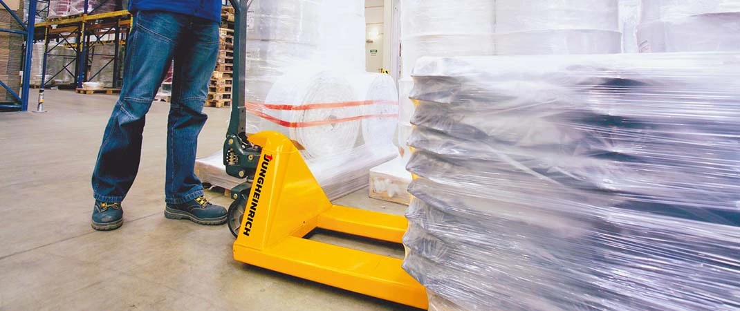 Ein Mann bewegt einen Hubwagen unter eine Palette mit folierter Ladung