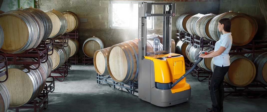 Frau transportiert Weinfässer mithilfe eines Hochhubwagens in einem Weinkeller